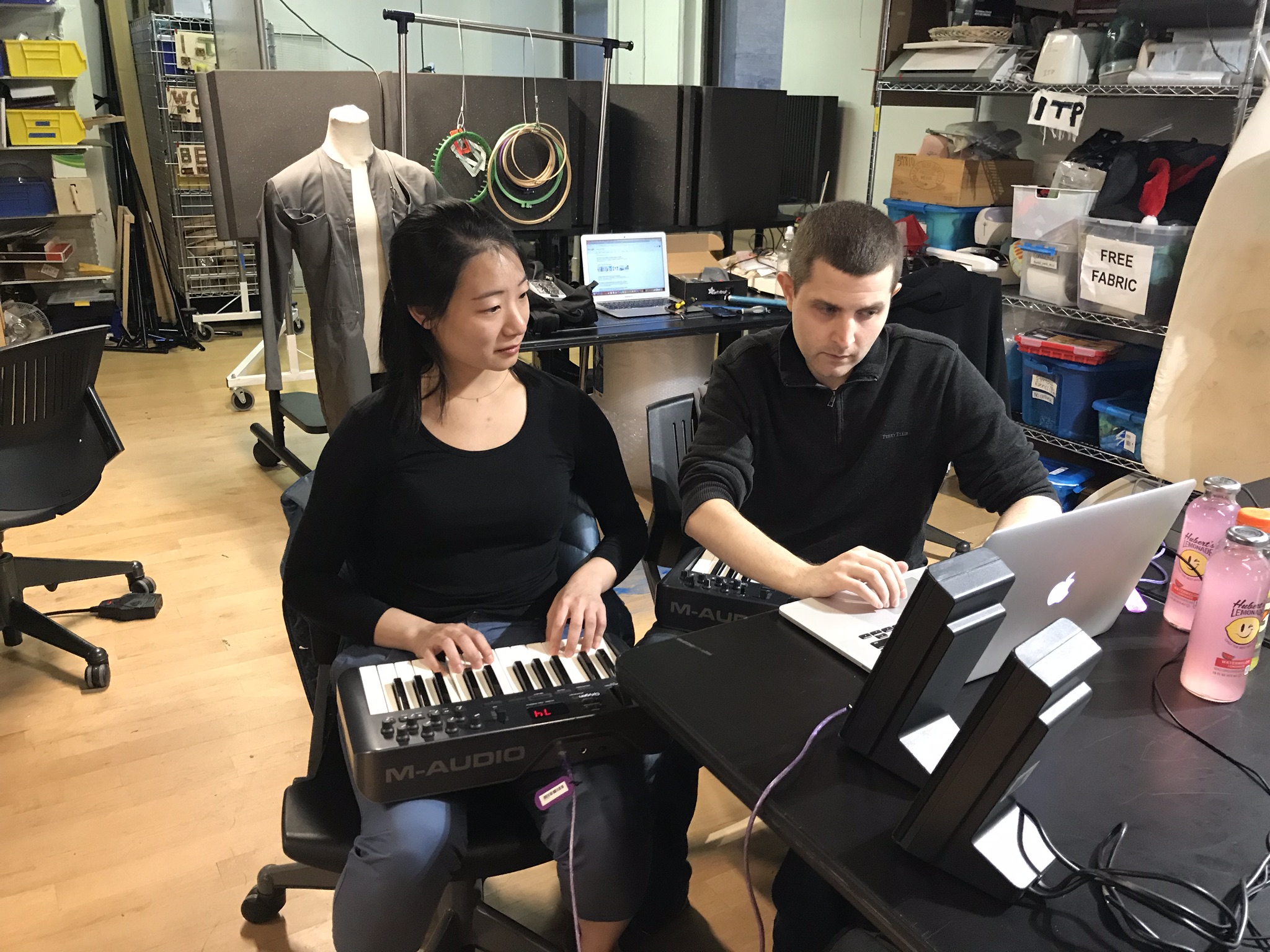 a woman and a man sitting in front of a computer, the woman has a keyboard on her lap